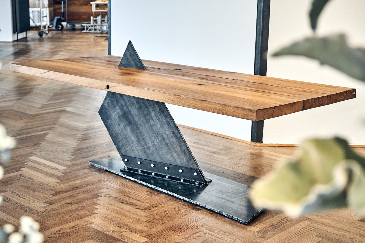 Tisch aus Altholz Eiche auf einem Fußgestell aus flachem Rohstahl mit Patina, welches den Tisch aufspießt und die Spitze über der Tischplatte heraussticht