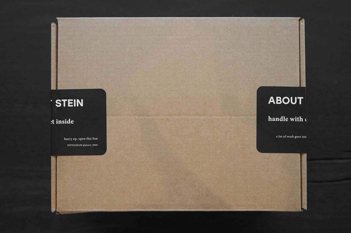 Karton, der an den Seiten mit einem schwarzen Aufkleber von About Stein zugeklebt ist