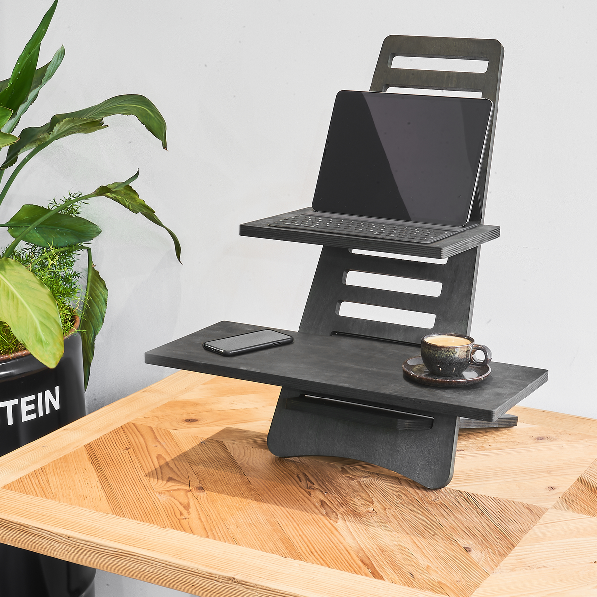 Aufgebauter schwarzer Stehtisch aus Holz auf einem Schreibtisch mit einer Tasse Kaffee, einem Tablet und einem Handy