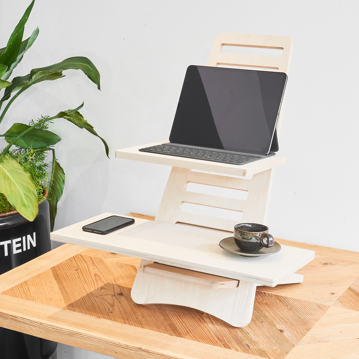 Aufgebauter heller Stehtisch aus Holz auf einem Schreibtisch mit einer Tasse Kaffee, einem Tablet und einem Handy